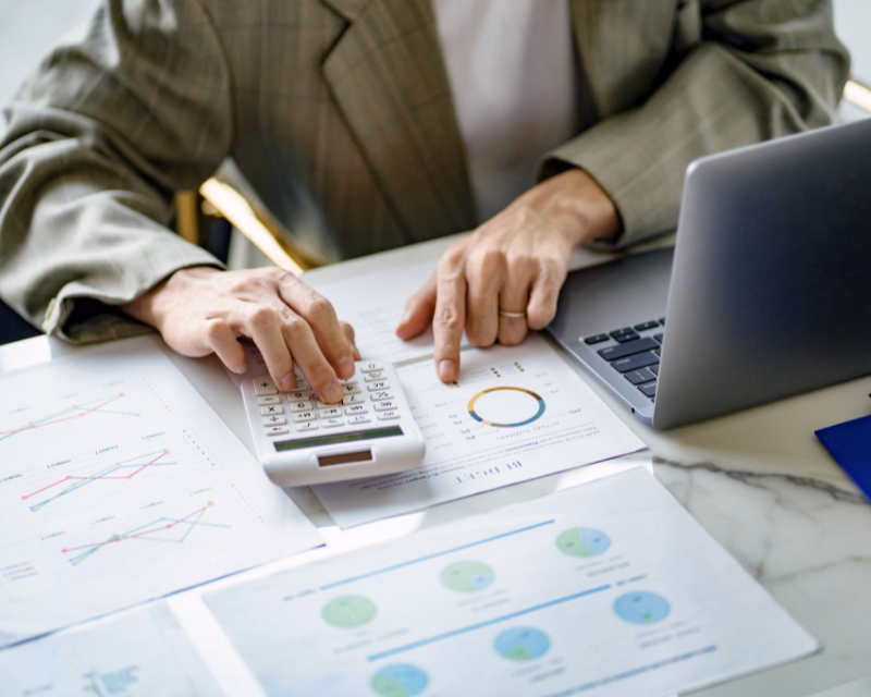 Financial report review concept image showing a calculator, laptop, and printed balance and performance reports during bookkeeping analysis