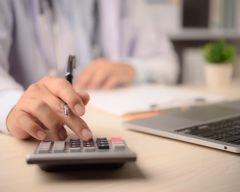 Income and expense review concept image showing a calculator, pen, paperwork, and laptop on an organized office desk during bookkeeping analysis