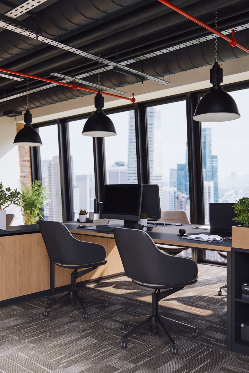 Modern office workspace with desks, chairs, computer monitors, and large windows in a clean professional setting