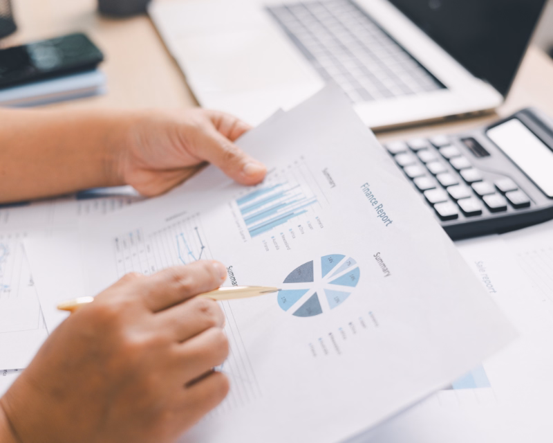 Findings summary concept image showing a hand pointing to a printed financial report beside a calculator and laptop during bookkeeping review