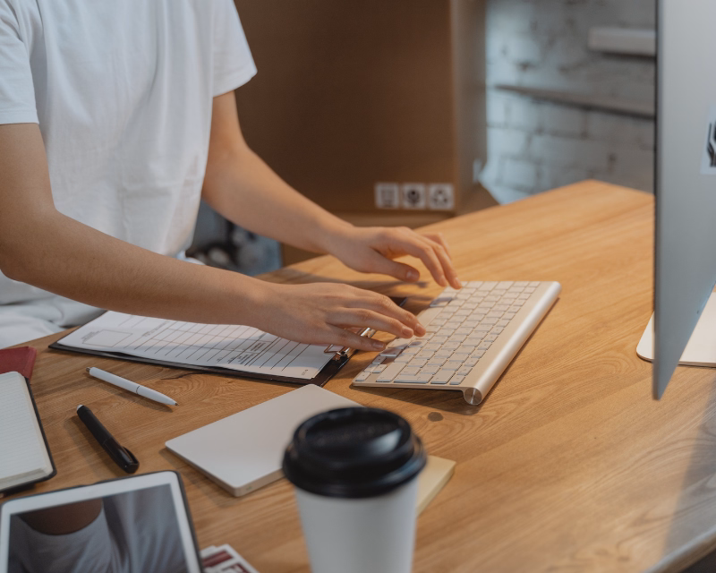 Bookkeeping cleanup workspace with hands sorting financial paperwork, a correction checklist, calculator, and a blurred desktop monitor on an organized desk