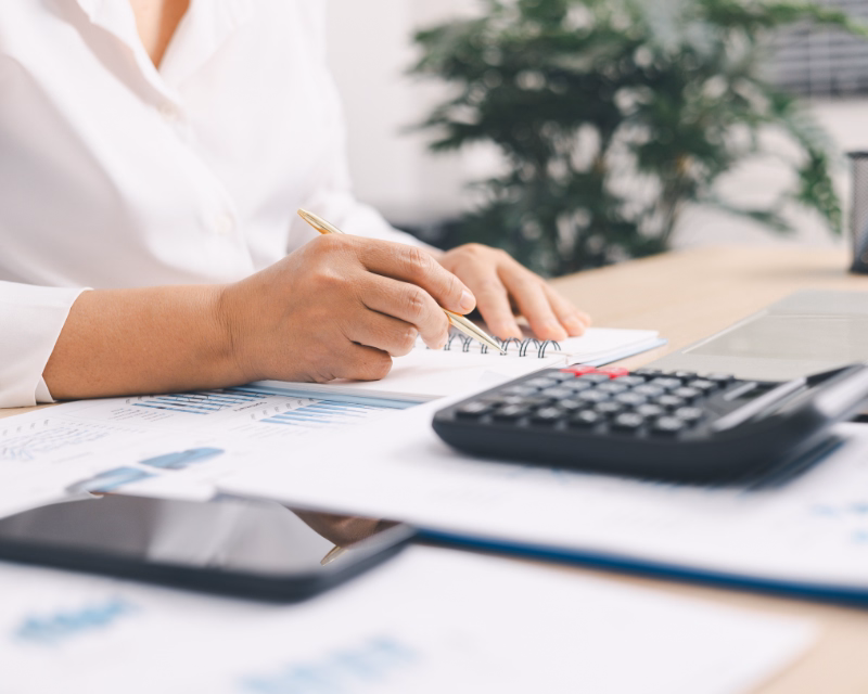 Business owner gathering monthly bookkeeping records with notes, a calculator, and financial reports on a desk.