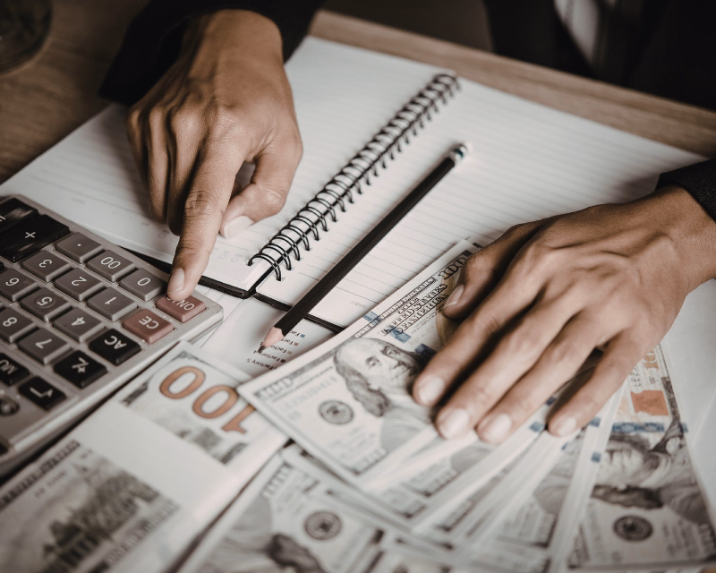 Hands reviewing cash with a calculator and notebook during monthly transaction tracking and bookkeeping.